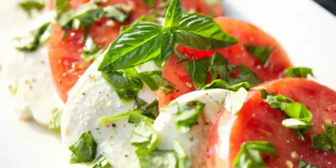 Salade Caprese : fines tranches de tomates rouges et de mozzarella crémeuse, parsemées de basilic frais. Une recette simple et savoureuse.