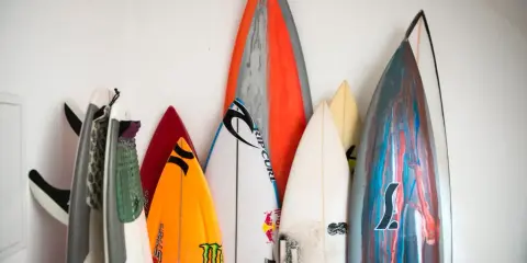 Eine Sammlung bunter Surfbretter steht an einer weißen Wand. Sie sind bereit für das nächste Abenteuer auf den Wellen beim Wellenreiten.