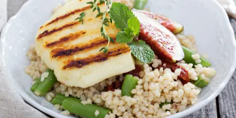 Kuskus z grillowanym serem halloumi, fasolką szparagową i figami, ozdobiony miętą.