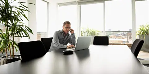 Mężczyzna w okularach rozmawia przez telefon, pracując na laptopie. Planuje koszty uzyskania przychodu 2025.