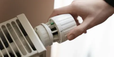 Hand dreht Thermostat einer Heizung. Energie sparen für die Gasheizung 2026.