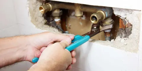 Mani con pinza lavorano su tubature in ottone. Si intravede una valvola di non ritorno prima o dopo la pompa, parte di un impianto idraulico.