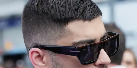 Mann mit stylischem Crew Cut und Sonnenbrille, der nachdenklich in die Ferne blickt.