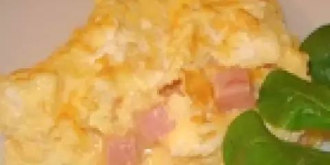 Une omelette jambon fromage dorée, garnie de dés de jambon rose et de fromage fondant, accompagnée de quelques feuilles vertes.