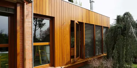 Modern house with ventanales grandes para casas, madera y ladrillo. Un árbol frondoso cuelga sobre la estructura.
