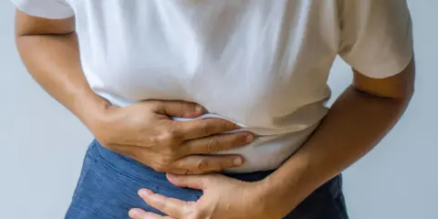 Person håller sig om magen, upplever smärta som kan vara relaterad till IBS och ont i ryggen.
