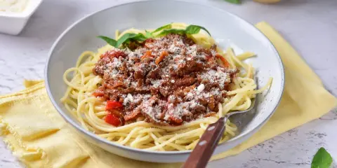 Pyszne spaghetti z bogatym sosem mięsnym na bazie passaty, posypane parmezanem i udekorowane listkami bazylii.