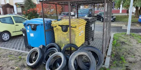 Kilka zużytych opon leży przed śmietnikami.