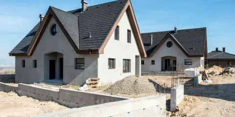 Nowe budynki usługowe z częścią mieszkalną w trakcie budowy. Widać fundamenty, materiały budowlane i dachy.