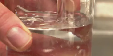 Main d'une personne tenant un verre d'eau potable à Poitiers. L'eau est claire et reflète la lumière.