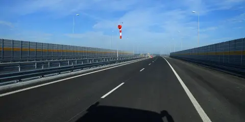 Pusta jezdnia nowej drogi z barierami dźwiękochłonnymi i wiatrowskazem.
