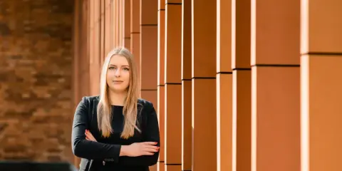 Kobieta w czarnym garniturze stoi na tle nowoczesnej fasady z pomarańczowymi elementami.