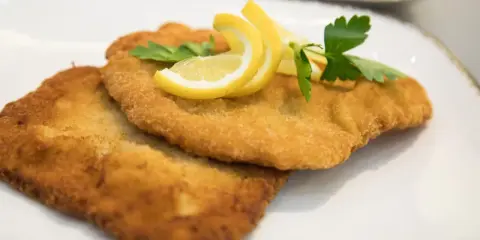 Zwei goldbraune Schnitzel, perfekt in Butter gebraten, garniert mit Zitronenspalten und Petersilie auf einem weißen Teller.