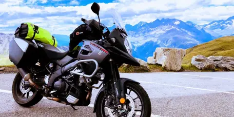 Szary motocykl Suzuki V-Strom, idealny motocykl do turystyki we dwoje, zaparkowany na tle majestatycznych gór i błękitnego nieba.