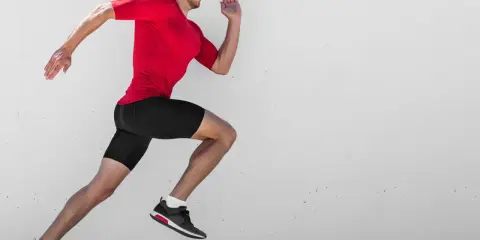 Ein Mann in rotem Shirt und schwarzen Shorts läuft mit hoher Kadenz gegen eine Betonwand.