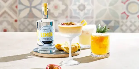 Erfrischender Vodka Sour mit Passionsfrucht und Zitrone, daneben ein weiterer Cocktail mit Ananas. Eine Flasche Zitronen-Wodka steht bereit.