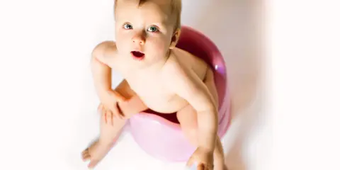 Bambino seduto sul vasino rosa, con espressione sorpresa. Attenzione alla cistite nei bambini.