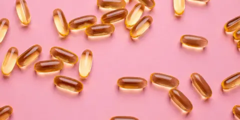 Capsule dorate sparse su sfondo rosa, utili per la vitamina D in gravidanza.