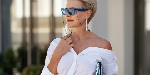 Elegancka starsza pani w okularach i białej koszuli, z biżuterią.