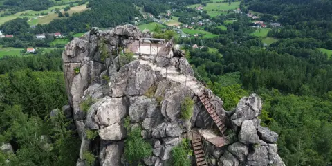 Widok z góry na skalny masyw Sokolik Duży, z platformą widokową i schodami prowadzącymi na szczyt. W tle zielone wzgórza i lasy.
