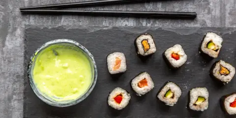 Sushi mit Lachs, Avocado und Paprika, dazu eine grüne Soße. Ist Wasabi gesund? Ja, es ist bekannt für seine entzündungshemmenden Eigenschaften.