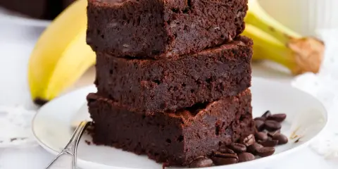 Stos puszystych brownie z bananami, ozdobiony ziarnami kawy, na talerzu z bananem w tle.