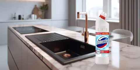 Domestos na zatkany zlew. Nowoczesna kuchnia z czarnym zlewem i złotą baterią, obok butelka Domestos.