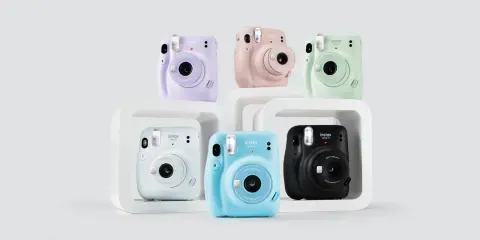 Pięć aparatów Instax Mini 11 w różnych kolorach: fioletowym, różowym, zielonym, białym, niebieskim i czarnym.