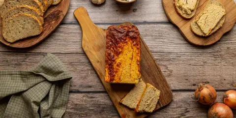 Domowy pasztet z mięsa z rosołu, pokrojony na desce, obok kromki chleba, cebule i czosnek.