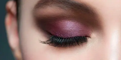Maquillaje de ojos con sombra morada brillante y pestañas largas, ideal para realzar la mirada en párpados caídos.