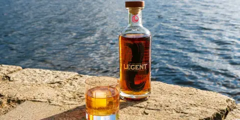 Legent Bourbon Whisky: Ein Glas und eine Flasche stehen auf einem Stein am Wasser. Was ist Bourbon Whisky? Ein Genuss für besondere Momente.