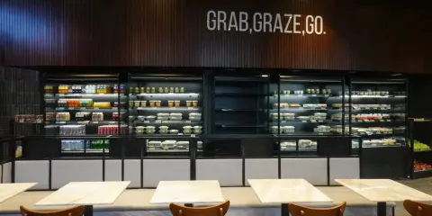 Refrigeradores llenos de comidas listas para llevar. El letrero "GRAB, GRAZE, GO" inspira una comida rápida y deliciosa.