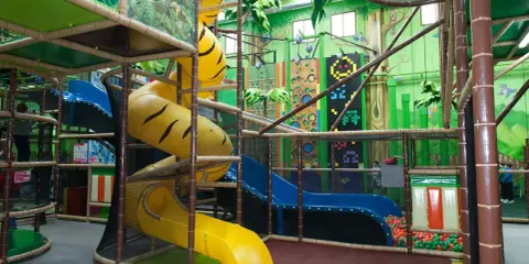 Un divertido parque infantil en Madrid con toboganes amarillos y azules, rocódromos y una piscina de bolas.