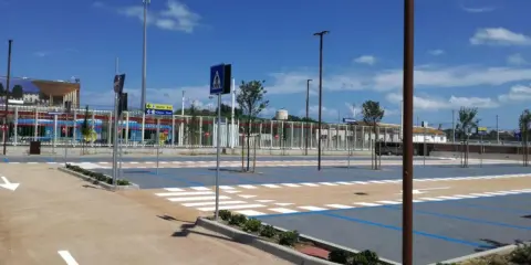 Parcheggio rimini con strisce pedonali e segnaletica, sullo sfondo un treno blu.