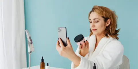 Kobieta w szlafroku sprawdza oryginalność kosmetyku za pomocą aplikacji na telefonie.