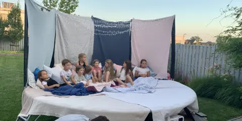 Dzieci siedzą na wielkim materacu pod gołym niebem, oglądając film. To idealne urodziny na dworze z magicznymi światełkami i wygodnymi kocami.