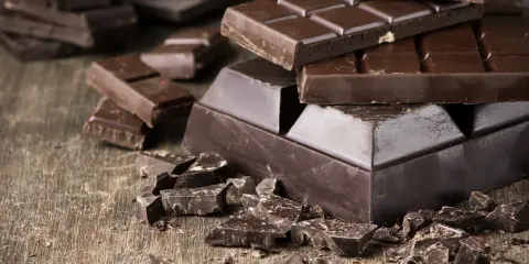 Des morceaux de chocolat noir, entiers et brisés, sur une table en bois. Une invitation à découvrir comment adoucir le chocolat noir pour une dégustation parfaite.
