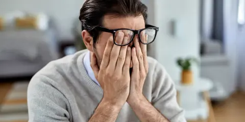 Mann mit Brille reibt sich die Augen, wirkt gestresst. Manche glauben, rauchen hilft gegen Stress, doch das ist ein Trugschluss.