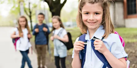Uśmiechnięta dziewczynka z plecakiem, gotowa na zmianę szkoły średniej w 2 klasie technikum. W tle jej koledzy i koleżanki.