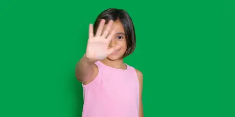 Niña de 4-5 años muestra timidez en niños, cubriendo su rostro con la mano.