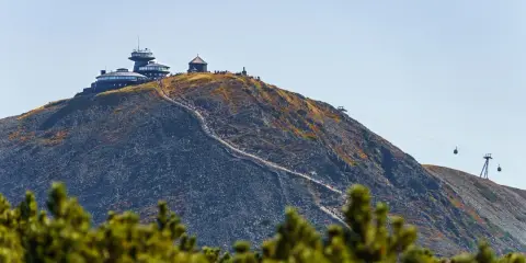 Szczyt Śnieżki w Karkonoszach, z obserwatorium i schroniskiem, po którym wije się ścieżka turystów. W tle kolejka linowa.