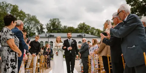 Para młoda idzie do ołtarza. W tle goście, którzy dokumentują uroczystość. To inspiracja, jak zorganizować skromny ślub cywilny.