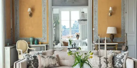 Ett elegant vardagsrum med fransk inredningsstil. Gyllene väggar, kristallkrona och antika möbler skapar en lyxig atmosfär.