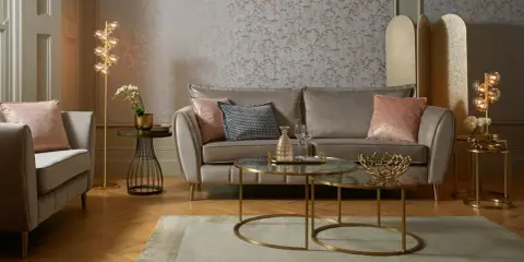 Przytulny salon glamour z beżową kanapą, różowymi poduszkami i złotymi dodatkami.