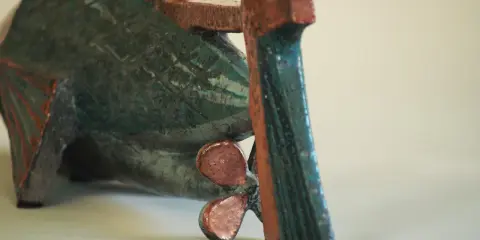 Sculpture de poisson en céramique, style Jean Derval, aux couleurs vives bleu-vert et rouge, avec une hélice visible.