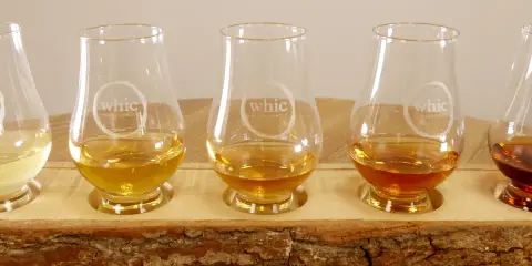Fünf Gläser mit unterschiedlichen Farben von **whiskey ohne farbstoff** stehen auf einem Holzbrett.