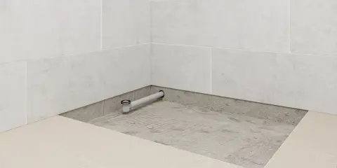 Installation d'un receveur de douche : un siphon est posé sur une chape avant le carrelage.