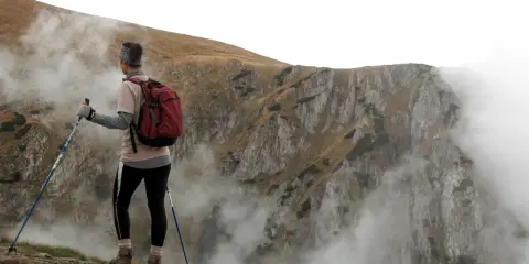 Person med ryggsäck och stavar, övar stavgång teknik på en bergssluttning med dimma.