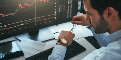 Un trader regarde sa montre, un chronophage qui le rappelle à l'ordre face aux graphiques boursiers.