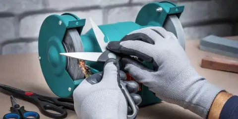 Manos enguantadas afilando tijeras de podar en una amoladora, chispas vuelan.